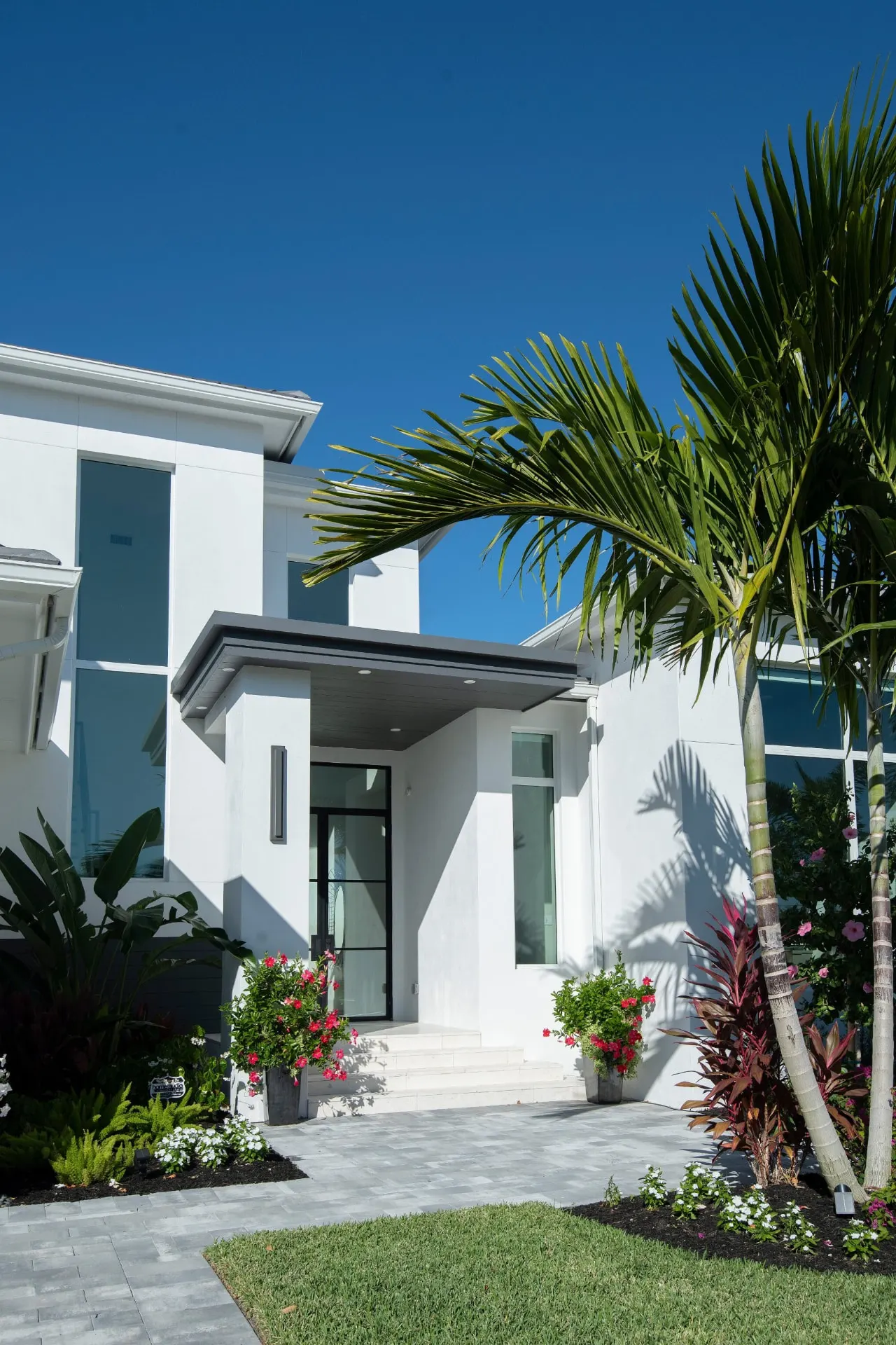 Entry of the Naples Park Residence with a dark canopy, black-framed glass doors, planters and a paver walkway.
