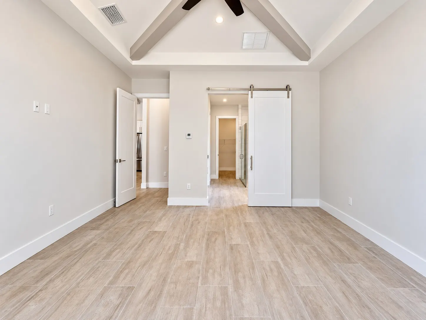 Primary bedroom with a vaulted beamed ceiling, tile wood-look floor, a barn door and an open walk-in closet beyond.