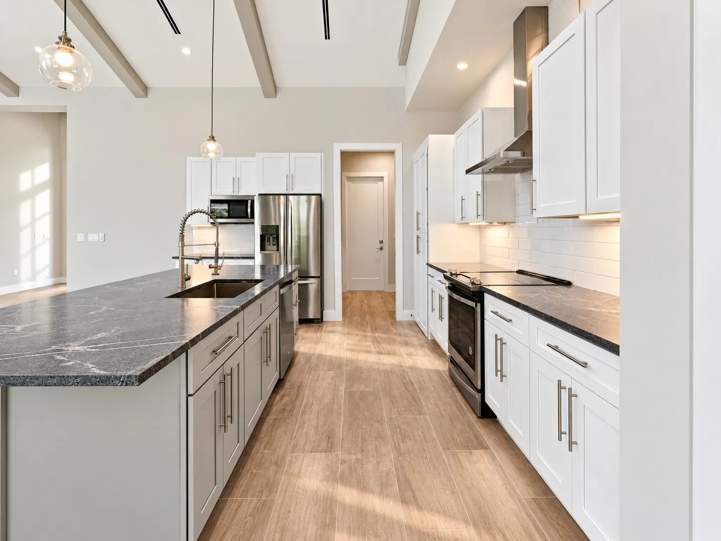 Kitchen with a long stone-top island, glass pendant lights, white cabinets and stainless steel appliances.