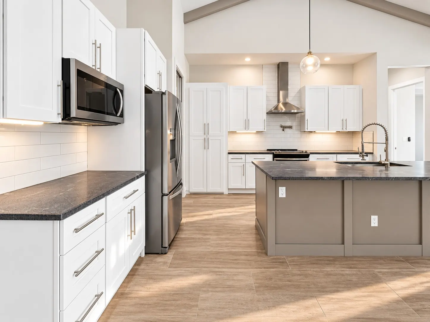 Kitchen under a vaulted ceiling with glass pendants, a range hood and a gray island.