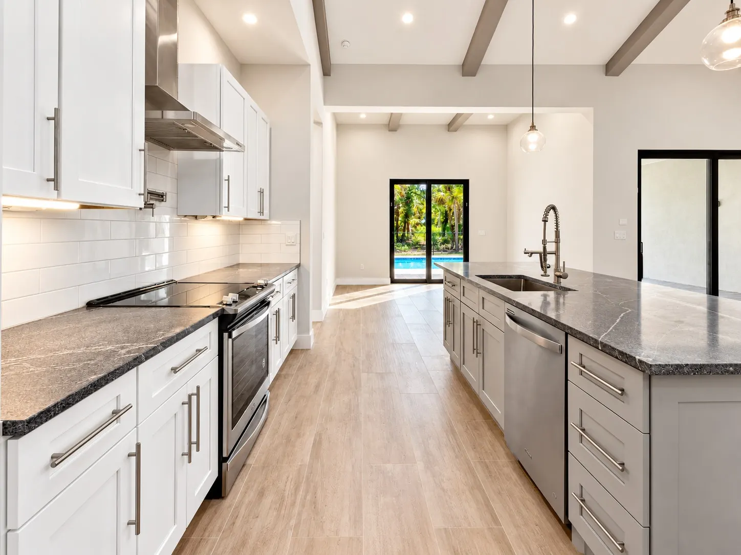Kitchen with white shaker cabinets, a gray island, black stone counters and a view through to sliding glass doors.