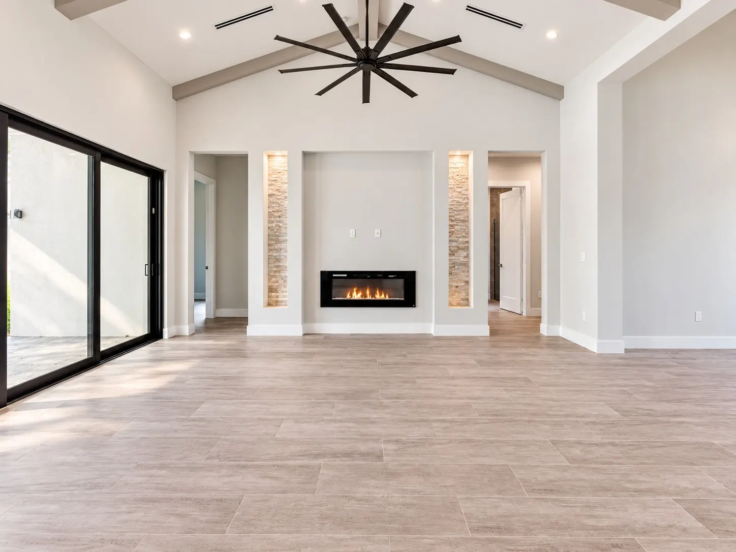 Living room with a vaulted ceiling, ceiling fan, linear fireplace flanked by stacked-stone niches and a large sliding glass door.