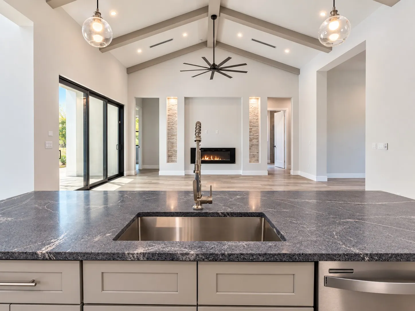 View across the kitchen island sink toward the fireplace wall and sliding doors in the great room.