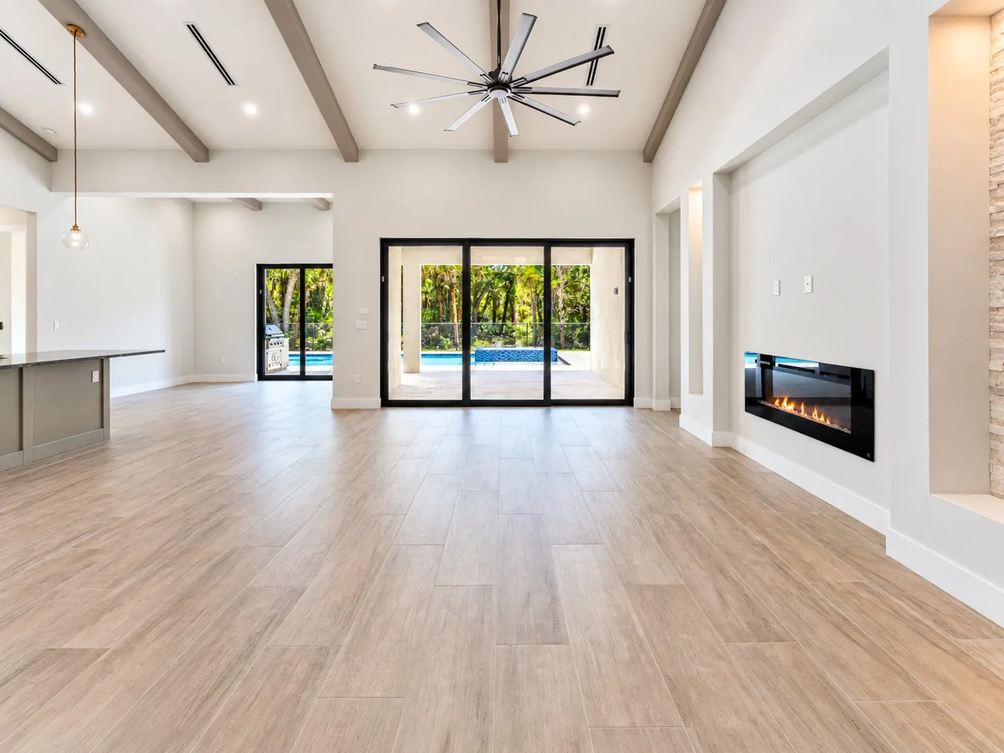 Great room with a vaulted beamed ceiling, a linear fireplace and sliding glass doors opening to the lanai and pool.
