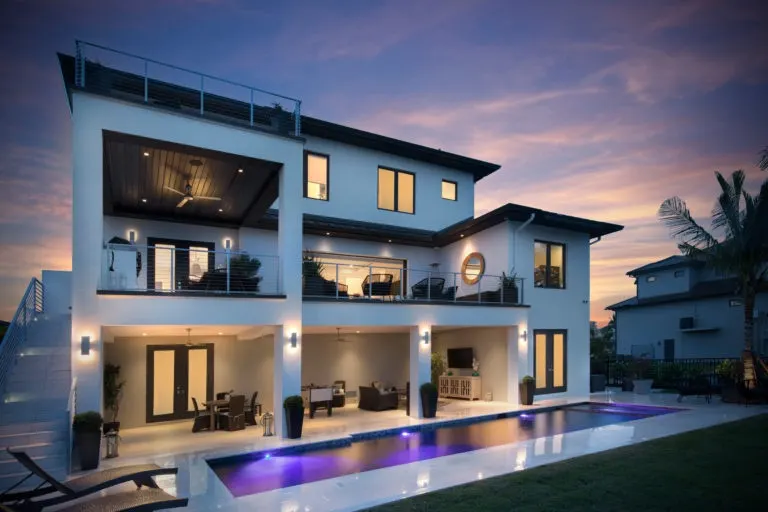 Rear of the home at dusk with multi-level covered terraces, cable railings and a lap pool lit in purple.
